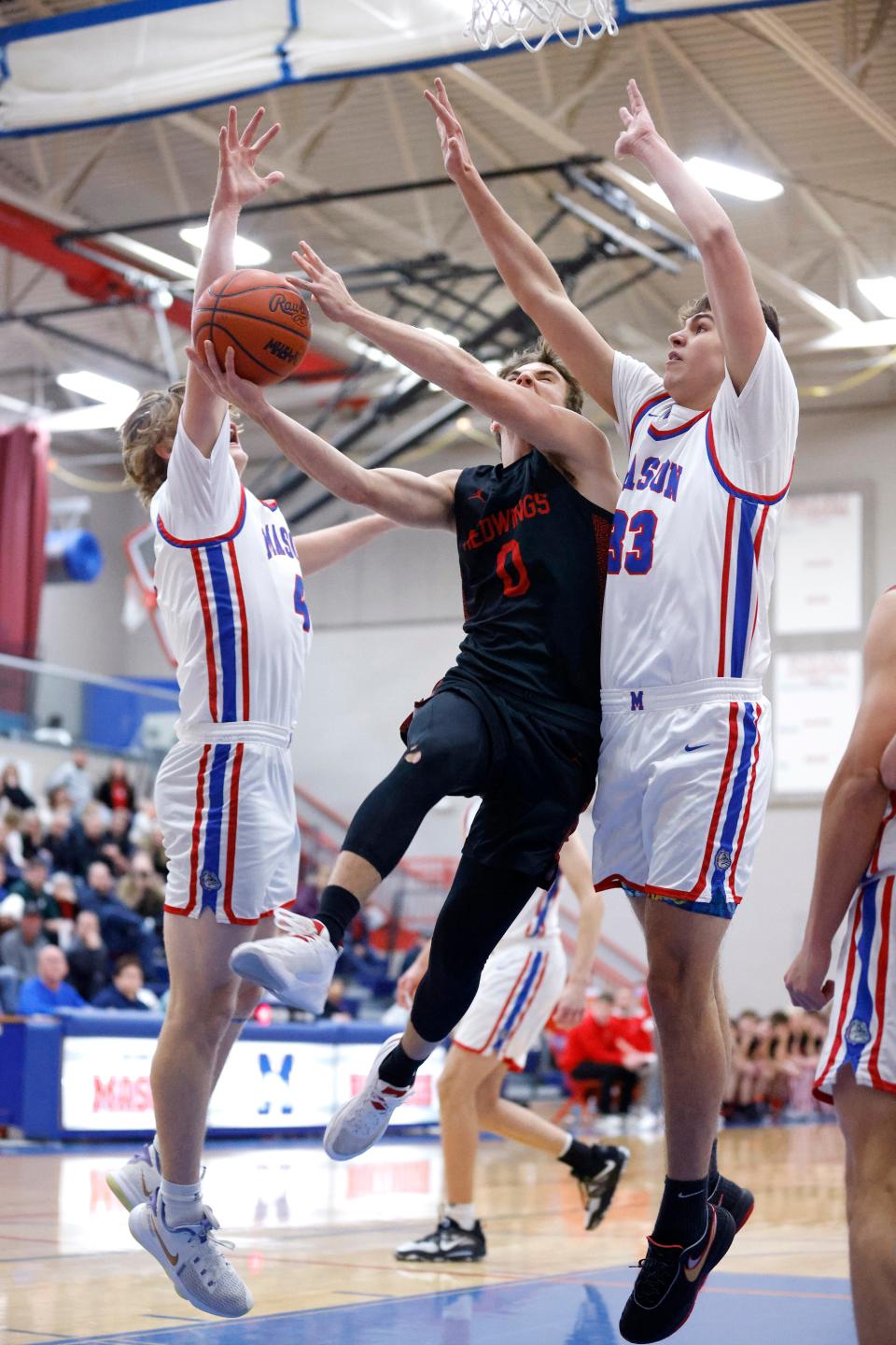 St. Johns' Carson Pieters, center, goes to the basket against Mason's Kaleb Parrish, left, and Austin Stone, Friday, Jan. 6, 2023, in Mason.