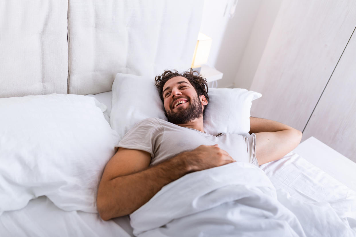 Young man sleeping waking up and stretching in his bed. people, bedtime and rest concept - man lying in bed at home, It's time to wake up