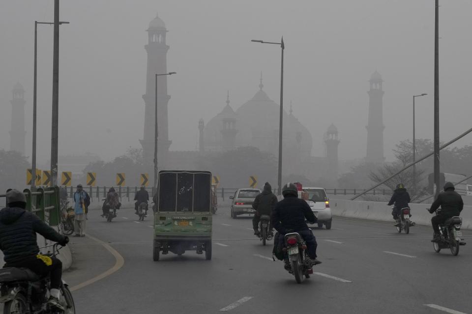 Motorcyclists and vehicles move on a bridge as smog envelops the historical Badshahi Mosque, background, in Lahore, Pakistan, Friday, Jan. 5, 2024. Lahore is in an airshed, an area where pollutants from industry, transportation and other human activities get trapped and cannot disperse easily. (AP Photo/K.M. Chaudary)