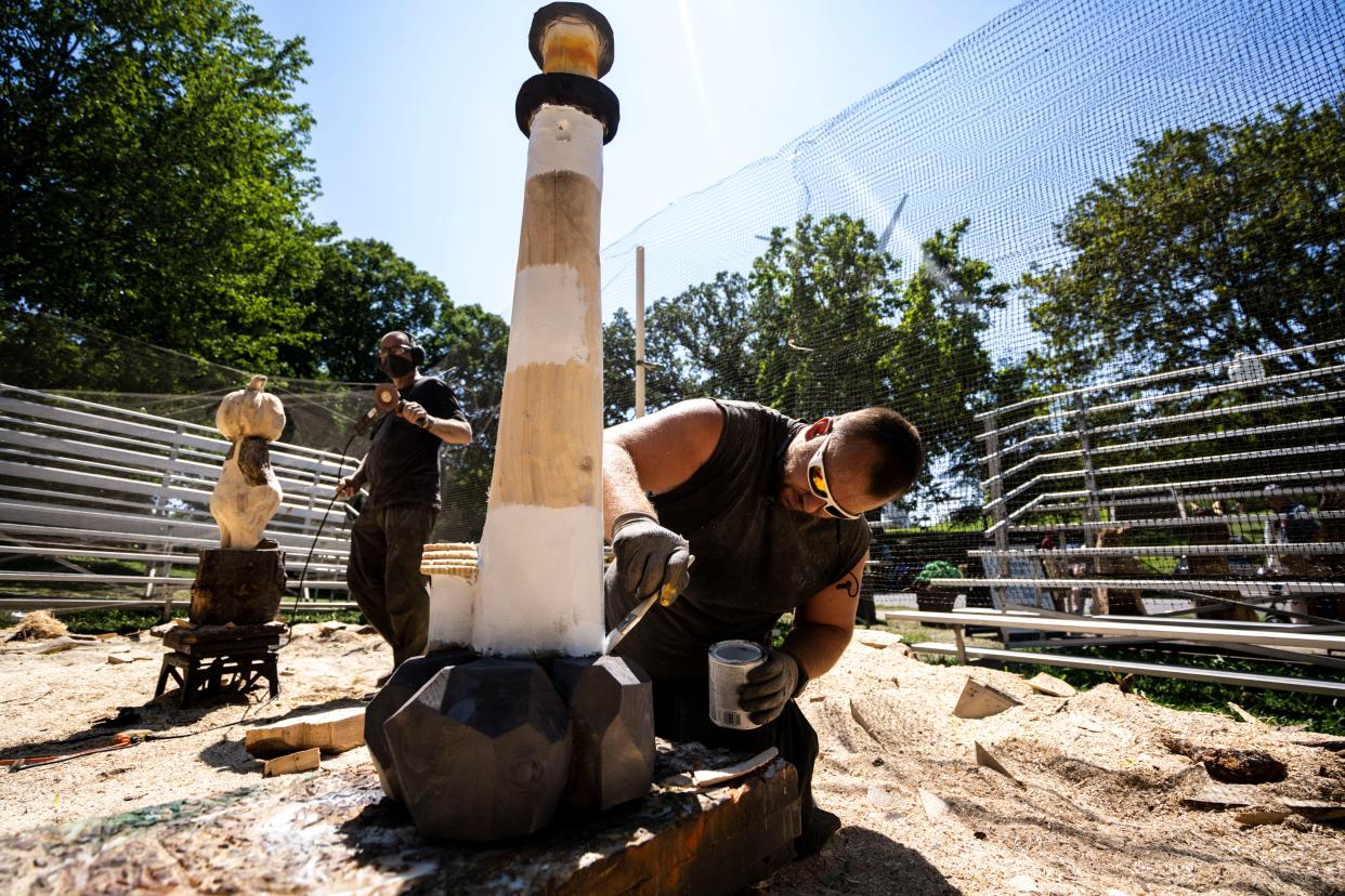 Chainsaw artist Clint Henik, of Mount Vernon, paints a lighthouse he carved at Heritage Village during day eight of the Iowa State Fair in 2023.