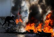 A demonstrator throws a tree branch on burning tires during ongoing anti-government protests in Tripoli