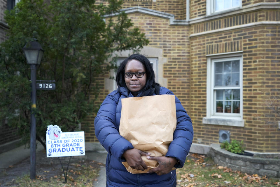 Briana Dominguez poses for a portrait outside her family's apartment building in Skokie, Ill., on Saturday, Nov. 21, 2020, holding the bag of groceries she received at the Hillside Food Pantry. “I never thought it would be me…” she says of her visits to the food bank in Evanston, Illinois. “But you do what you gotta do to survive.” (AP Photo/Charles Rex Arbogast)