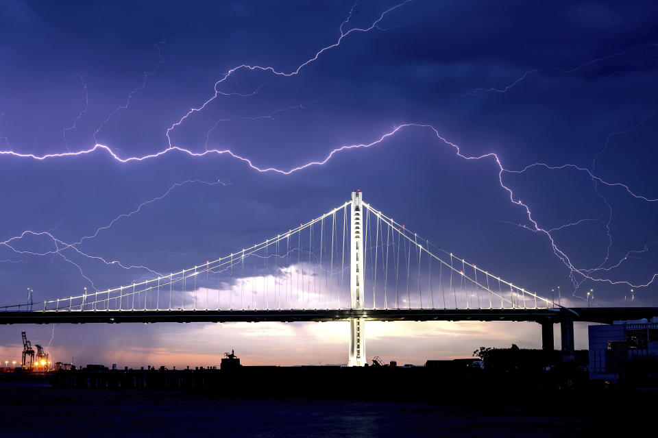 FILE - In this Aug. 16, 2020, file photo, lightning forks over the San Francisco-Oakland Bay Bridge as a storm passes over Oakland, Calif. Numerous lightning strikes sparked brush fires throughout the region. (AP Photo/Noah Berger, File)