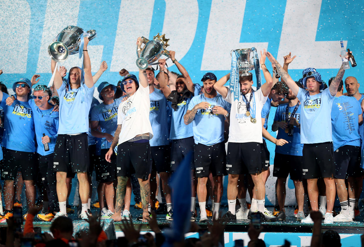 Manchester City players celebrate on stage with their Treble trophies.