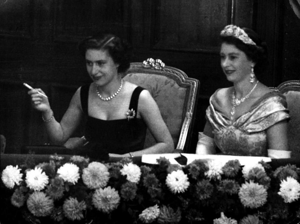 Their eyes riveted on the stage, Queen Elizabeth II, right, and her sister, Princess Margaret, smoking a cigarette, watch the Royal Variety Performance from the Royal Box at the Palladium, London.   (Photo by PA Images via Getty Images)