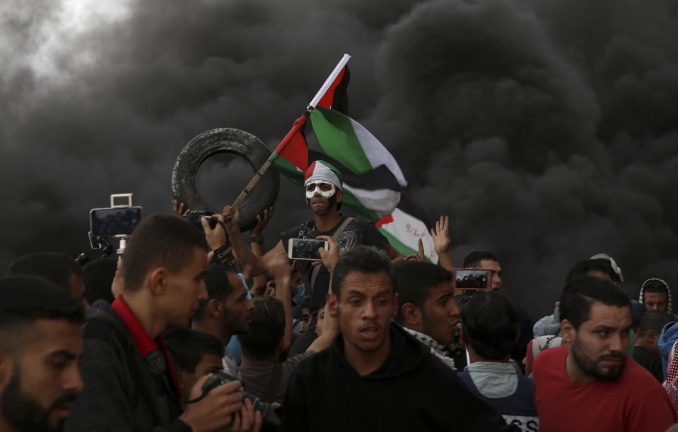 Protesters chant slogans while waves their national flags as others burn tires near the fence of the Gaza Strip border with Israel during a protest east of Gaza City, Friday, Oct. 26, 2018. (AP Photo/Adel Hana)