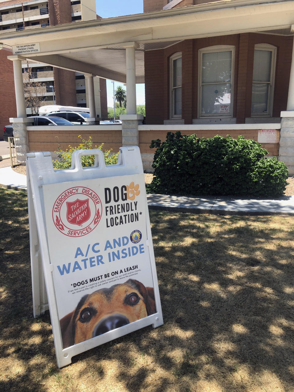 A sign board welcoming people to bring their dogs sits out front at the Salvation Army Phoenix downtown headquarters where a heat relief station was set up on Thursday, May 28, 2020, in Phoenix, Ariz. The heat relief station offering cold water and a cool place inside to rest out of the brutal sun will be open every day through Sunday while an excessive heat warning is in effect. (AP Photo/Anita Snow)