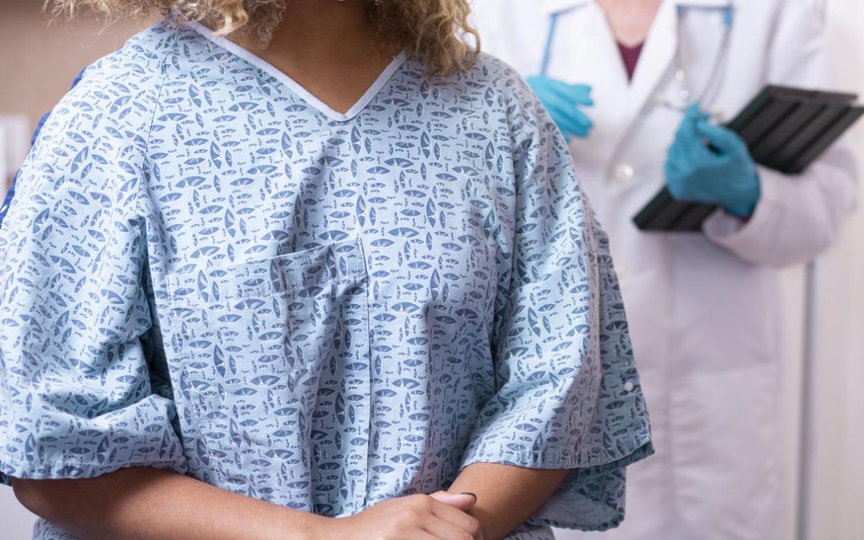 Young African American woman prepares for a breast exam, mammogram from her gynecologist doctor at hospital or clinic. Women's health issues. Breast Cancer awareness.