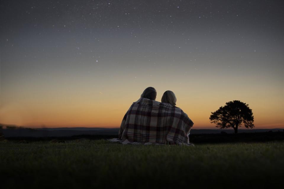 a mature couple sitting wrapped in a blanket looking at the night sky full of stars