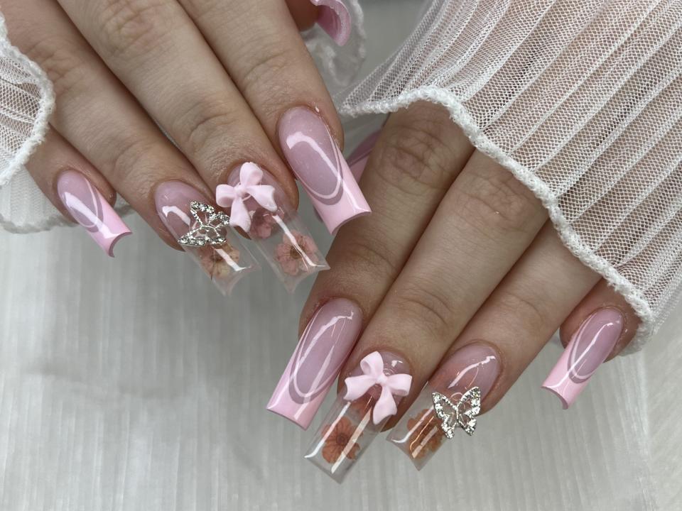 hands with long acrylic nails in square shape and French tip design. Added 3D Bow and encapsulated flower.