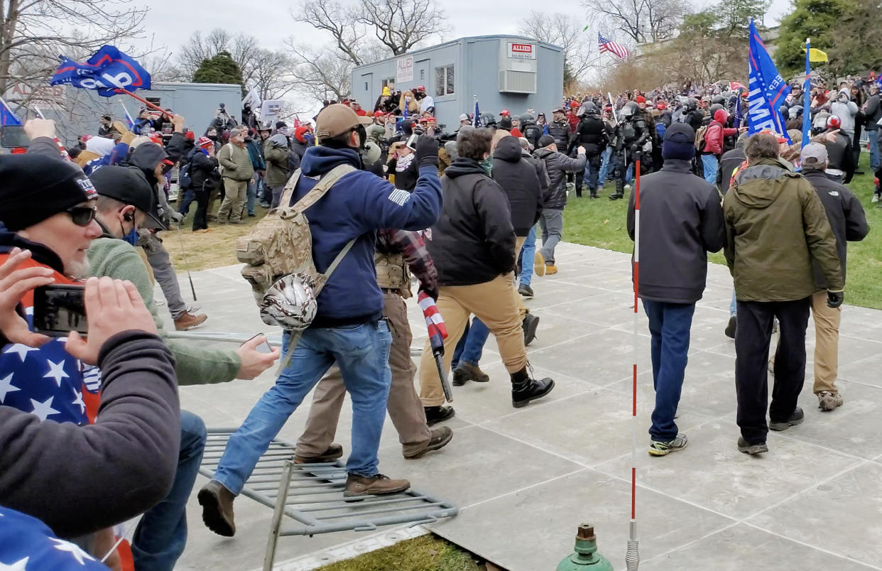 Image: Derek Kinnison, wearing a blue sweatshirt, steps on a police barrier as he approaches the  Capitol on Jan. 6, 2021. (U.S. District Court)