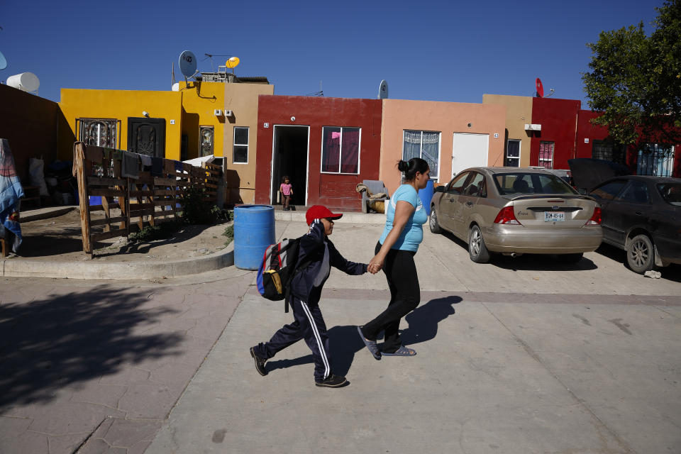In this Jan. 28, 2020, photo, Ruth Aracely Monroy, right, rushes her son, Nahum Perla, left, to school from their home on the outskirts of Tijuana, Mexico. They were among the first sent back to Mexico under a Trump administration policy that dramatically reshaped the scene at the U.S.-Mexico border by returning migrants to Mexico to wait out their U.S. asylum process. (AP Photo/Gregory Bull)