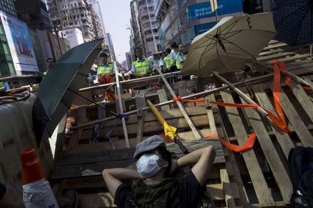 A pro-democracy protester sleeps on a barricade as police stand guard behind him on a blocked road at Mongkok shopping district in Hong Kong October 18, 2014. REUTERS/Tyrone Siu