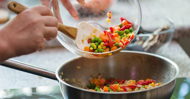 young woman cooking at home, preparing Spanish seafood paella with shrimp, mussels, octopus, and vegetables