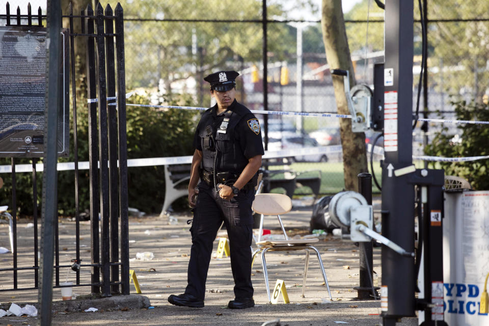 FILE - In this July 28, 2019 file photo, a police officer walks by yellow evidence markers at a playground after a shooting in the Brownsville neighborhood in the Brooklyn borough of New York. New York City police have made an arrest in the community festival shooting that left one person dead and 11 wounded this summer. Police said Wednesday, Oct. 16, that 20-year-old Kyle Williams, of Brooklyn, was arrested on murder, criminal possession of a weapon, reckless endangerment and attempted murder charges. (AP Photo/Mark Lennihan, File)