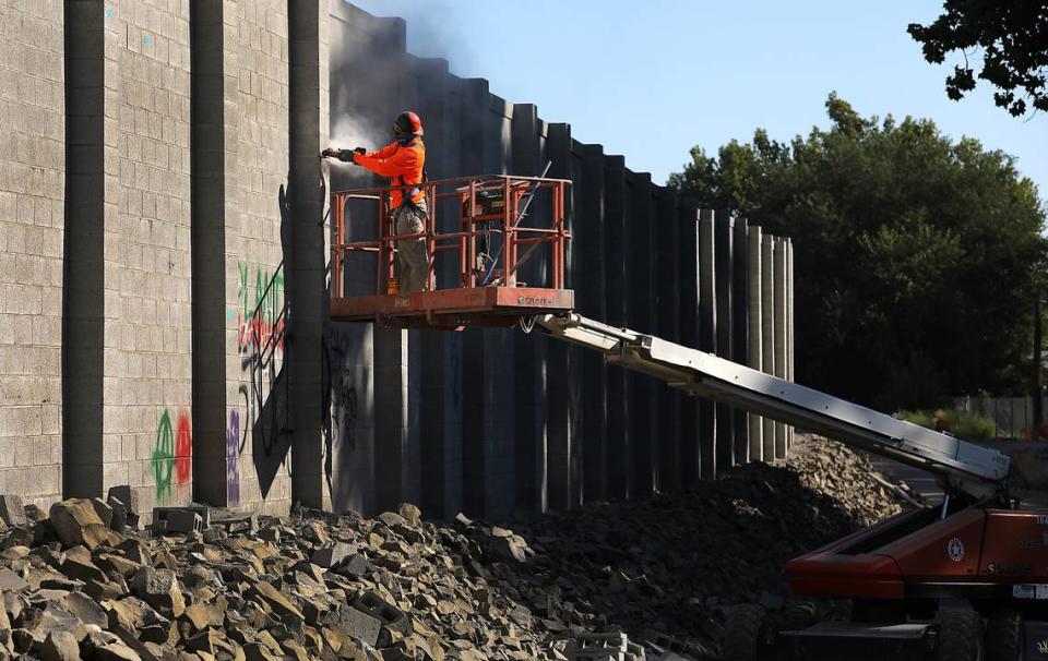 A construction worker makes final adjustments to mobile home park side of the wall above several sections marked with spray paint.