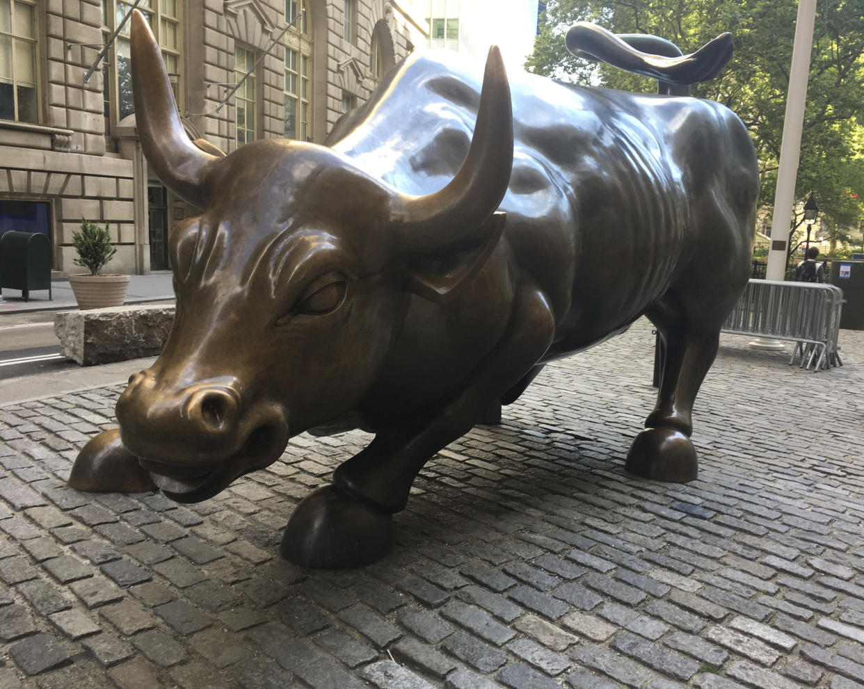 A bronze sculpture of a charging bull is shown on cobblestones near the New York Stock Exchange.