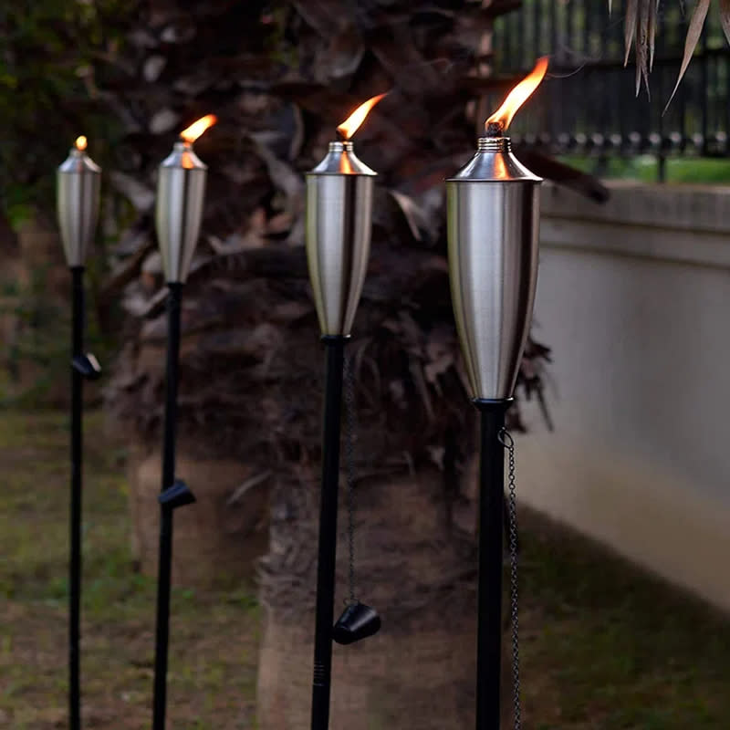 Four lit torches on stands in a garden at dusk