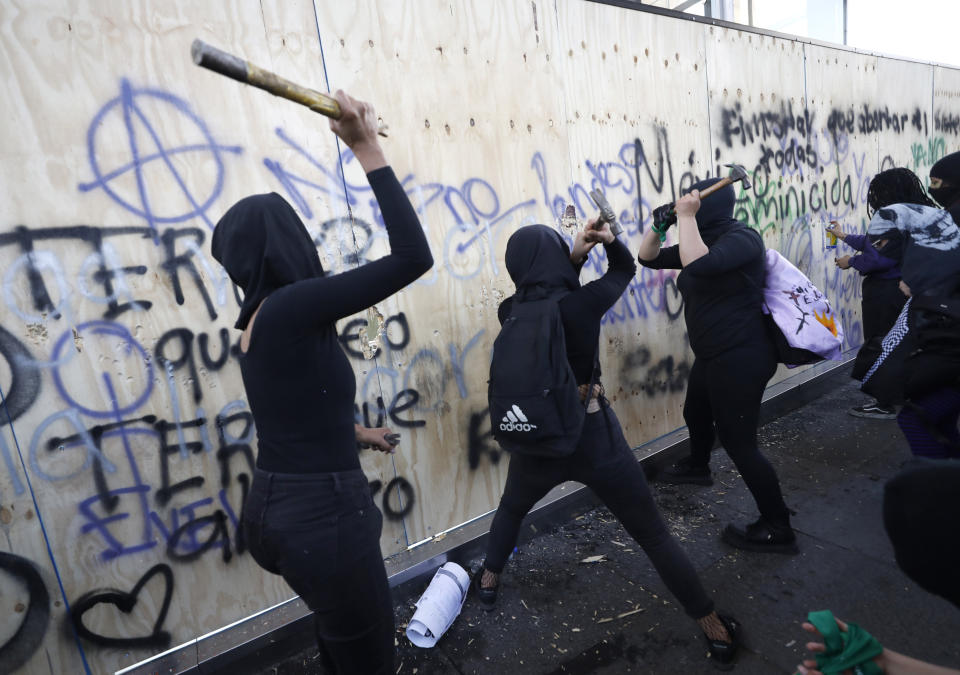 Women attack a wooden wall protecting Mexico's Revolution Monument during a march to commemorate International Women's Day and protest against gender violence, in Mexico City, Monday, March 8, 2021. (AP Photo/Rebecca Blackwell)