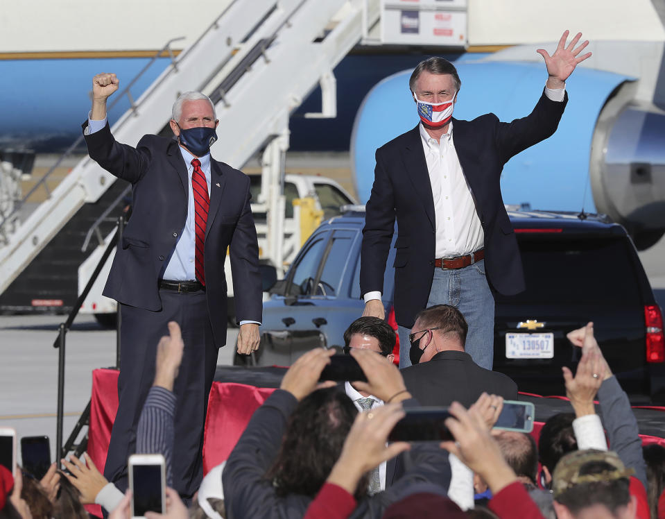 Vice President Mike Pence, left, and Sen. David Perdue, R-Ga., react to cheering supporters at the conclusion of Pence's Defend the Majority Rally following remarks on the accomplishments of the Trump Administration and the Republican Senate Majority and stumping for Sens. Kelly Loeffler and Perdue, Thursday, Dec. 10, 2020, in Augusta, Ga. (Curtis Compton/Atlanta Journal-Constitution via AP)