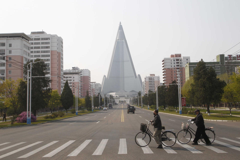 People wearing face masks cross a road in front of the Ryugyong Hotel in Pyongyang, North Korea Tuesday, April 28, 2020. (AP Photo/Cha Song Ho)