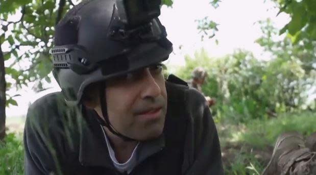 CBS News correspondent Imtiaz Tyab takes cover under a tree in a village near Kherson, Ukraine, with his team and Ukrainian forces as Russian shells land nearby, in late May, 2022. / Credit: CBS News