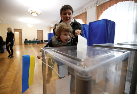 A woman holds a child, who casts a ballot at a polling station during the second round of a presidential election in Kiev, Ukraine April 21, 2019. REUTERS/Vasily Fedosenko