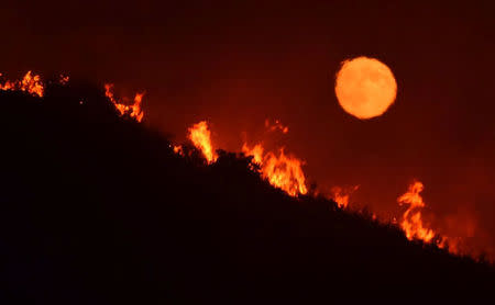 The full moon rises over flames of the Alamo fire on a hilltop off Highway 166 east of Santa Maria, California, July 7, 2017. Mike Eliason/Santa Barbara County Fire Dept/Handout via REUTERS