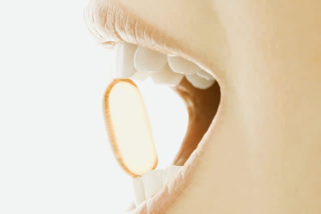 Woman holding vitamin soft gel capsule between teeth, close-up