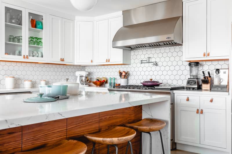 A white kitchen with cookware stored on the stove and the kitchen island