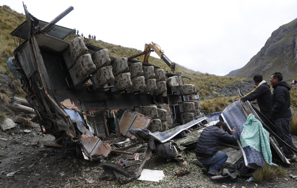 People look at the remains of a bus that crashed in Inca Chaca, outskirts of La Paz, Bolivia, Friday, Jan. 31, 2020. At least fourteen people died and several were injured after the bus drove off a mountain road and fell down a ravine.. (AP Photo/Juan Karita)
