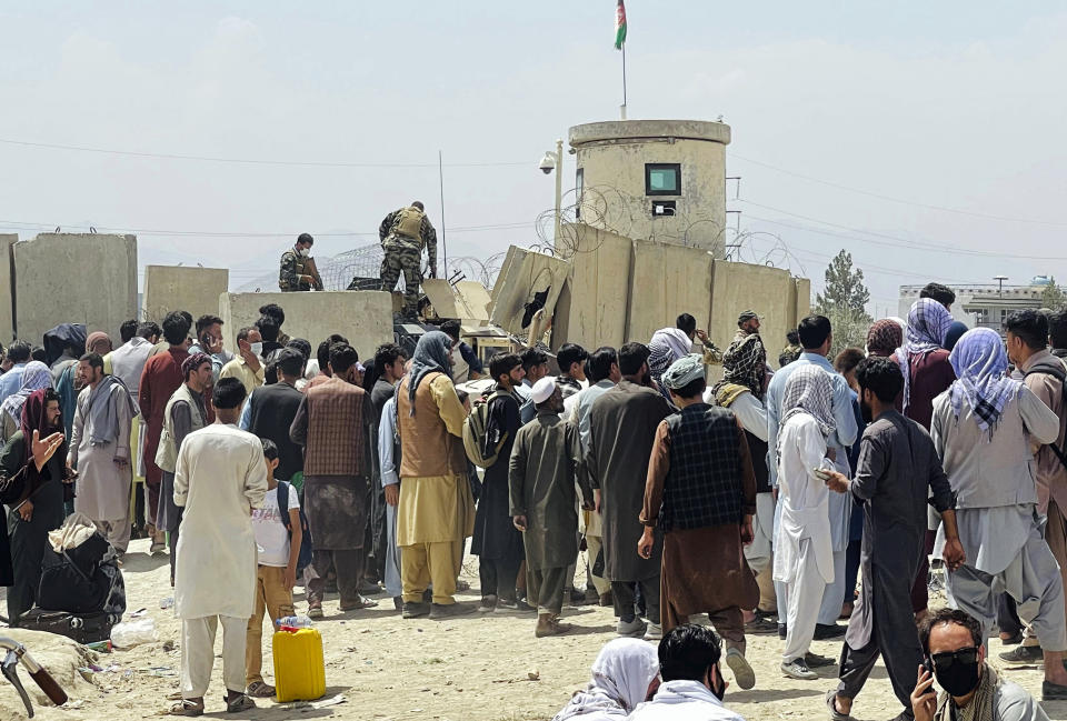 Afghan security guards stand on a wall as hundreds of people gather outside the international airport in Kabul, Afghanistan, Tuesday, Aug. 17, 2021. The Taliban declared an “amnesty” across Afghanistan and urged women to join their government Tuesday, seeking to convince a wary population that they have changed a day after deadly chaos gripped the main airport as desperate crowds tried to flee the country. (AP Photo)