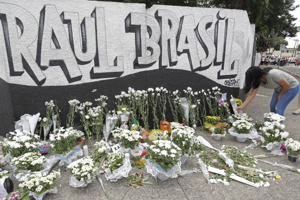 A woman leaves flowers one day after a mass, school shooting outside the Raul Brasil state school in Suzano, Brazil, Thursday, March 14, 2019. Classmates, friends and families began saying goodbye on Thursday, with thousands attending a wake in the Sao Paulo suburb while authorities worked to understand what drove two former students to attack the Raul Brasil State School with a gun, crossbows and small axes. (AP Photo/Andre Penner)