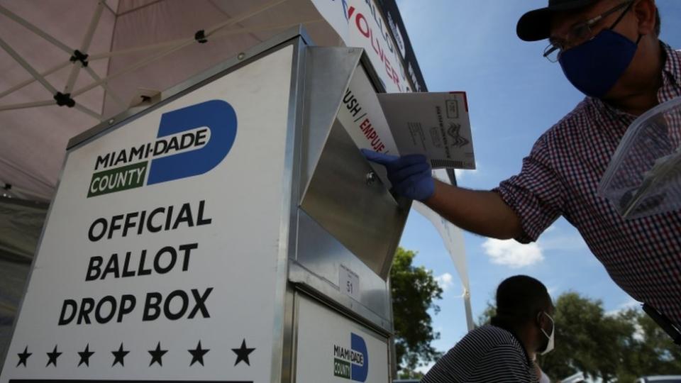 Un hombre con mascarilla inserta su voto en un buzón del correo para las elecciones en Estados Unidos.