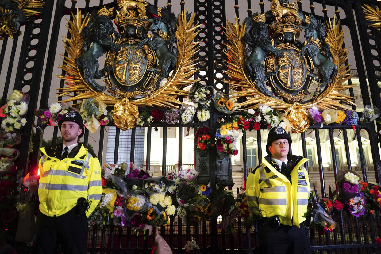 Police officers stand amongst floral tributes left outside Buckingham Palace. (Victoria Jones / PA via AP)