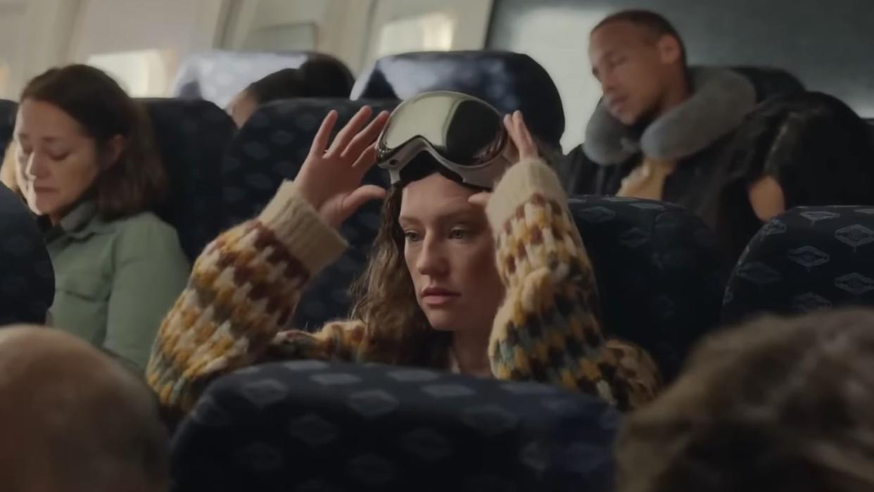  A woman wearing the Apple Vision Pro while on a plane with other passengers next to them. 