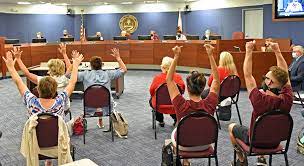 Members of the public raise their hands in protest at a Sarasota County School Board meeting.