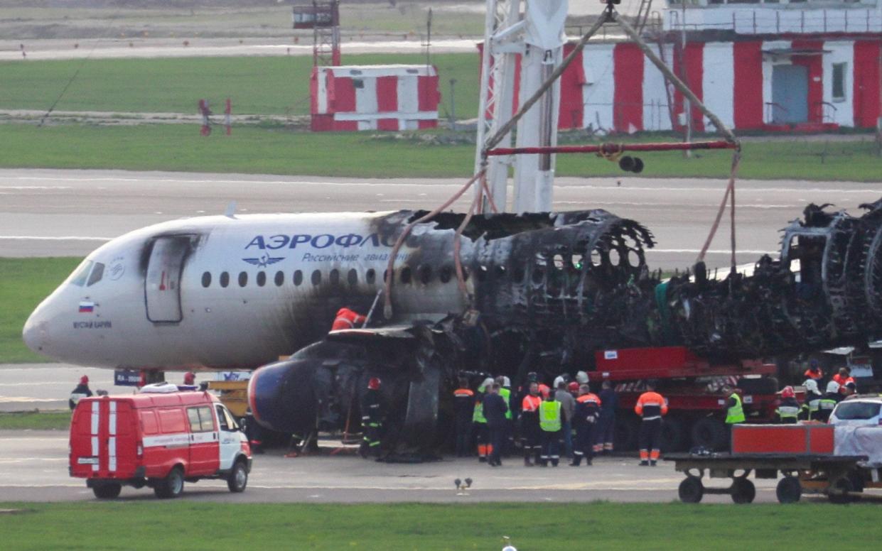 Workers remove the Sukhoi Superjet 100, which caught fire during an emergency landing after a lightning strike, from the runway on Monday - TASS / Barcroft Media