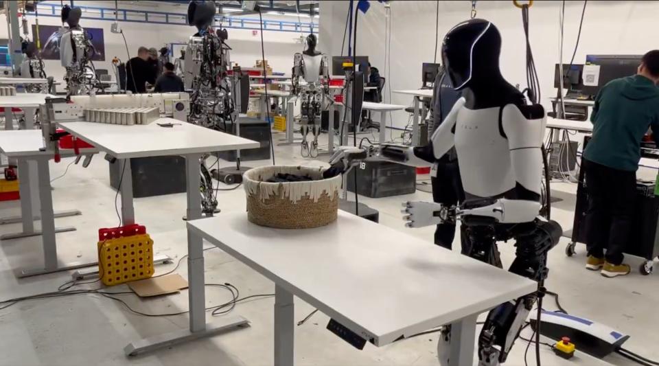 Several humanoid robots at workstations dangling mid-air at Tesla's Optimus lab