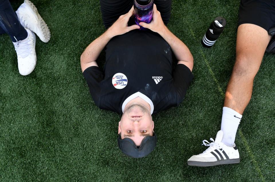 Blind soccer player Cody Kirchner lies on the pitch with his goggles resting on his forehead and takes a water break