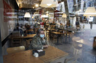 A woman sits in a cafe in Milan, Italy, Tuesday, Oct. 13, 2020. Italian Premiere Giuseppe Conte ordered strict new anti-COVID measures early Tuesday, including limits on private gatherings and a ban on casual pickup sports. Bars and restaurants must close at midnight, and drinks can only be consumed at tables -- not standing at the bar or outside -- after 9 p.m. (AP Photo/Luca Bruno)