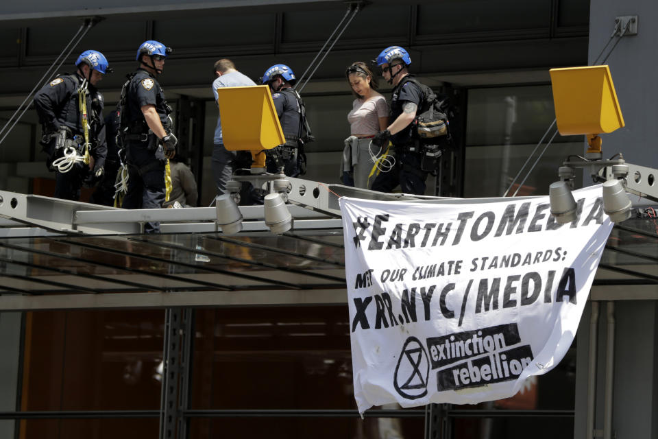 New York Police officers take into custody activists who climbed on the awning of the New York Times building to hang signs during a climate change rally, Saturday, June 22, 2019, in New York. Activists blocked traffic along 8th Avenue during a sit-in to demand coverage of climate change by the newspaper. (AP Photo/Julio Cortez)