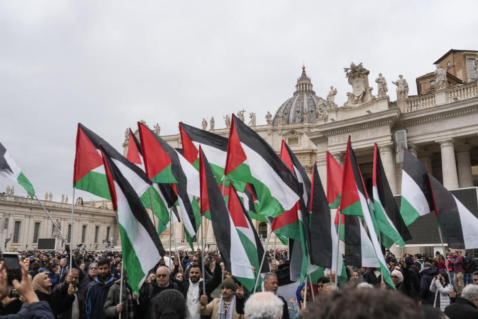 Palestinian flags are waived as people gather to see Pope Francis delivering the Urbi et Orbi (Latin for 'to the city and to the world' ) Christmas' day blessing from the main balcony of St. Peter's Basilica at the Vatican, Monday Dec. 25, 2023. (AP Photo/Gregorio Borgia)