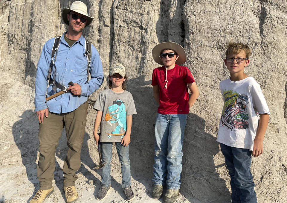 In this photo provided by Giant Screen Films, vertebrate paleontologist Tyler Lyson, left, poses with young fossil finders Liam Fisher, Jessin Fisher and Kaiden Madsen on the day their expedition uncovered diagnostic features of a juvenile T. rex the boys discovered in the Badlands of North Dakota. A documentary film caught the moment of discovery on camera. (David Clark/Giant Screen Films via AP)