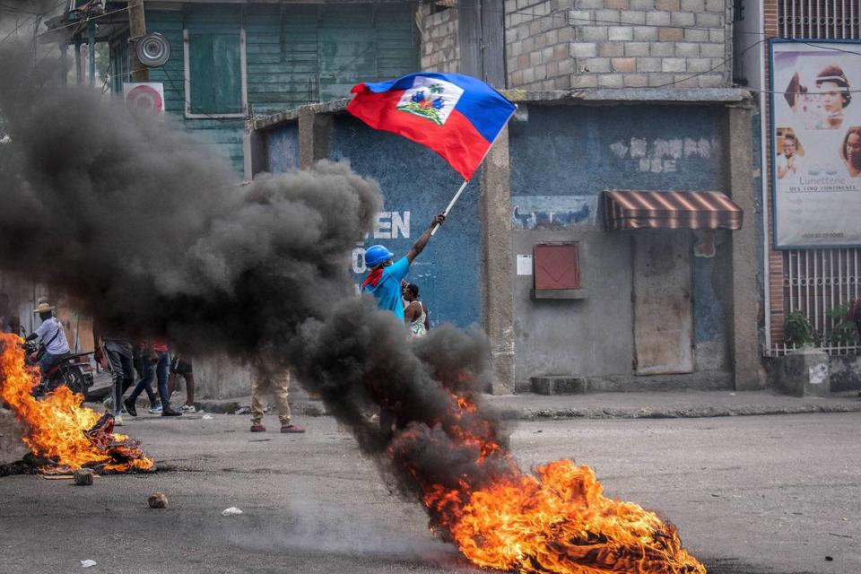 En una foto del 14 de agosto de 2023, un hombre con la bandera de Haití en la mano se para en medio de un incendio para pedir la paz. Haití se ha acercado al colapso total en los últimos días.