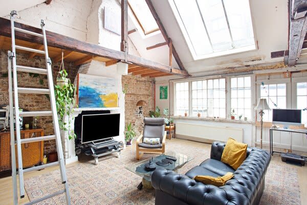 Expansive windows and skylight draw in an abundance of sunshine, which reflects off the exposed brick and wooden beams. A ladder leads to a cozy bedroom on the top level.