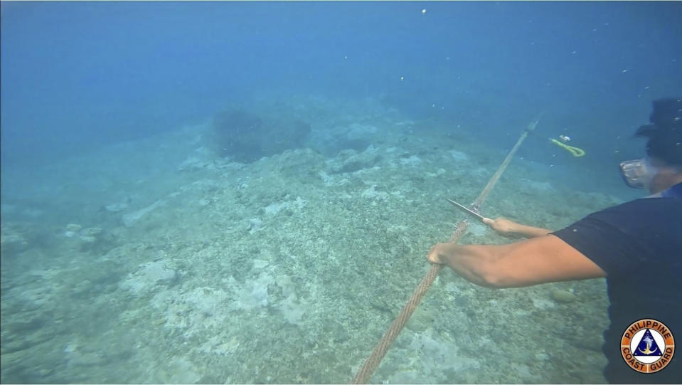 This undated photo provided on Sept. 26, 2023, by Philippine Coast Guard shows a diver cutting rope tied to a floating barrier in the Scarborough Shoal. The Philippine coast guard said Monday, Sept. 25, it has complied with a presidential order to remove a floating barrier placed by China’s coast guard to prevent Filipino fishing boats from entering a lagoon in a disputed shoal in the South China Sea.(Philippine Coast Guard via AP)