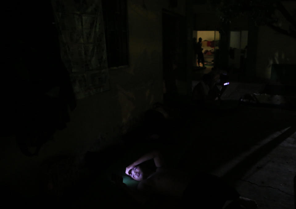 A migrant's face is illuminated by the light from his cell phone as he goes to bed on a mattress in the garden of the Good Shepherd migrant shelter in Tapachula, Mexico, Tuesday, June 18, 2019. Religious groups, mostly Catholic but including some Protestant denominations, have long operated shelters to aid migrants. (AP Photo/Rebecca Blackwell)