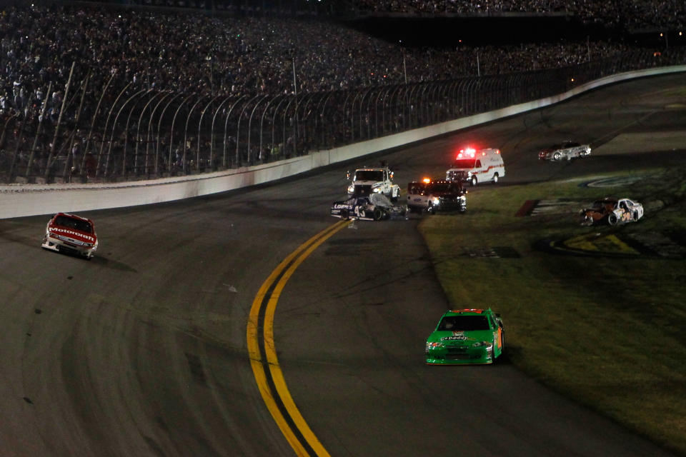 DAYTONA BEACH, FL - FEBRUARY 27: Safety workers tend to Jimmie Johnson, driver of the #48 Lowe's Chevrolet, as Danica Patrick, driver of the #10 GoDaddy.com Chevrolet, drives back on to the race track after being involved in an on track incident during the NASCAR Sprint Cup Series Daytona 500 at Daytona International Speedway on February 27, 2012 in Daytona Beach, Florida. (Photo by Jonathan Ferrey/Getty Images for NASCAR)