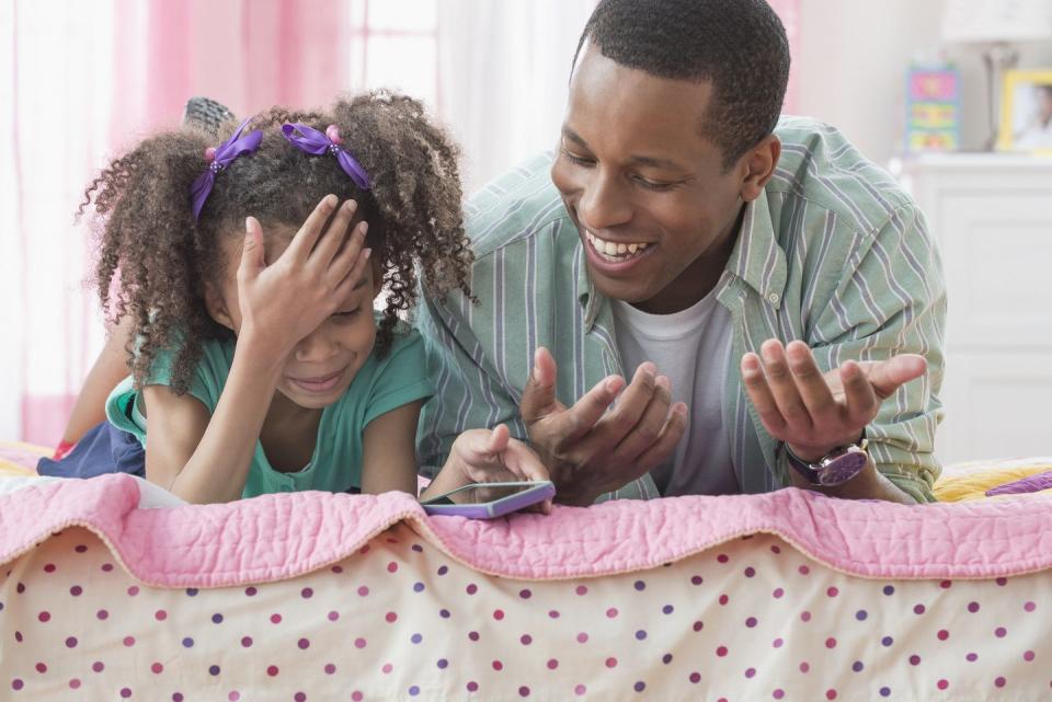 father and daughter using cell phone together on bed